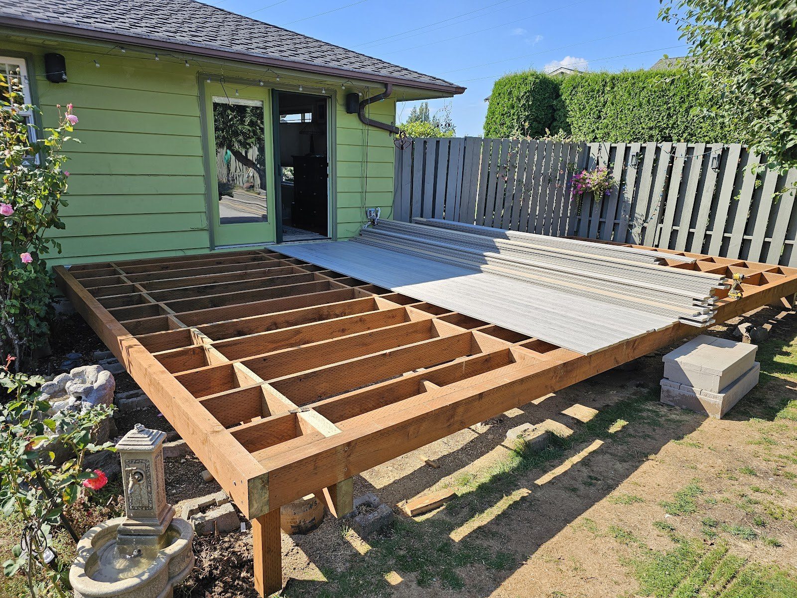 New deck framing set on posts beside a green home